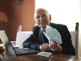 happy senior businessman holding money in hand while working on laptop at table